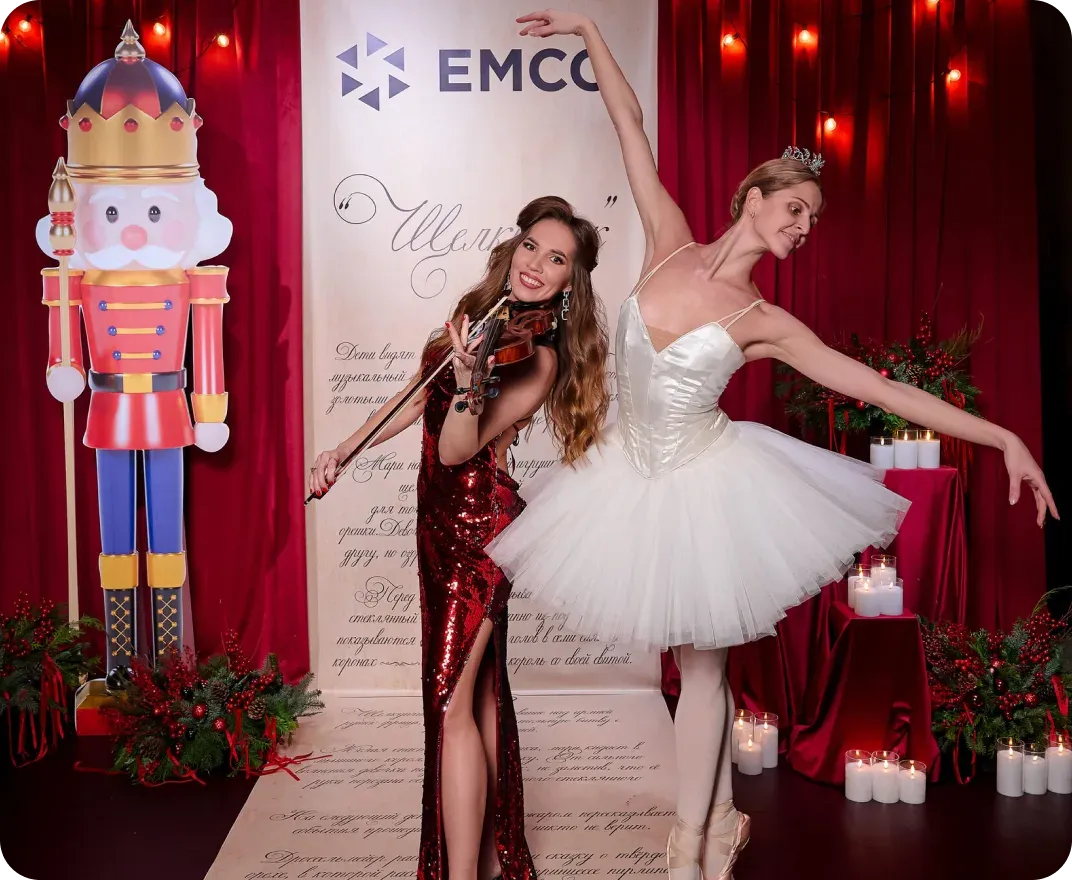 Скрипачка в красном платье и балерина у пресс-волла EMCO рядом с фигурой щелкунчика